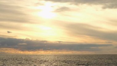 Golden sunset cloudy sky reflecting on calm ocean waters with ripples. Golden hour sunlight bathing calm ocean waves, soft clouds diffusing warm orange glow across expansive seascape. Calm atmosphere.