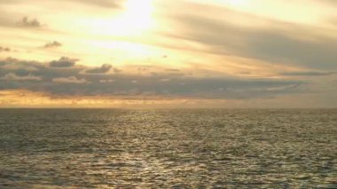 Golden sunset cloudy sky reflecting on calm ocean waters with ripples. Golden hour sunlight bathing calm ocean waves, soft clouds diffusing warm orange glow across expansive seascape. Calm atmosphere.