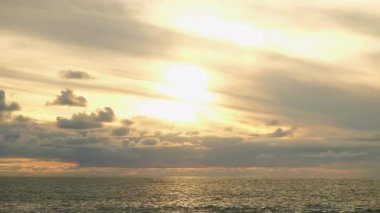 Golden sunset cloudy sky reflecting on calm ocean waters with ripples. Golden hour sunlight bathing calm ocean waves, soft clouds diffusing warm orange glow across expansive seascape. Calm atmosphere.