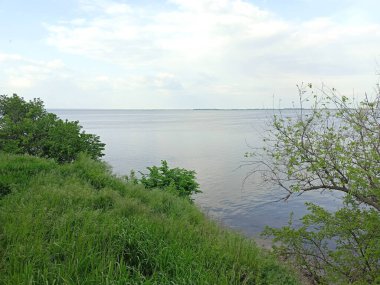 Samara Nehri 'nin durgun su yüzeyinin panoraması, ufuktaki uzak adaların arka planında, bulutlu, güneşli gökyüzünü yansıtıyor..