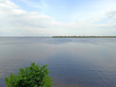 Samara Nehri 'nin durgun su yüzeyinin panoraması, ufuktaki uzak adaların arka planında, bulutlu, güneşli gökyüzünü yansıtıyor..