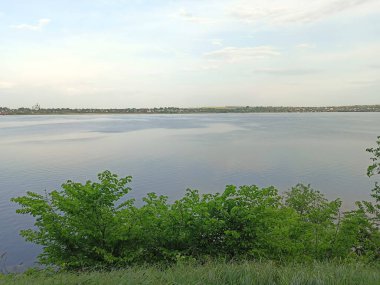 Samara Nehri 'nin su aynasının doğal bir görüntüsü yoğun kıyı bitki örtüsü prizmasından geçen bulutlu, güneşli bir gökyüzünün arka planına karşı..