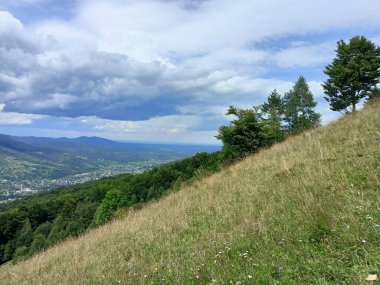 Dağ sırasının tepesinde uzanan küçük bir patikanın manzarası ve ufuktaki dağ geçidinde görülebilen bir yerleşim yerine götürüyor..