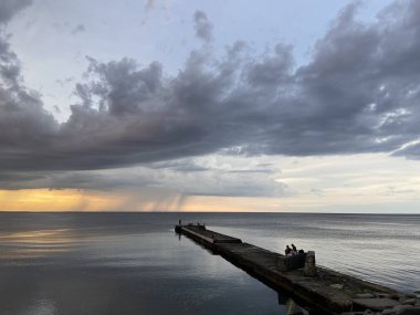 Uzun taştan bir dalgakıran denizin derinliklerine doğru yol alır, sanki deniz ufkunda sarı-sıcak günbatımına uzanır gibi..
