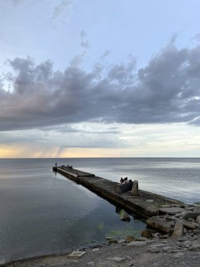 Uzun taştan bir dalgakıran denizin derinliklerine doğru yol alır, sanki deniz ufkunda sarı-sıcak günbatımına uzanır gibi..