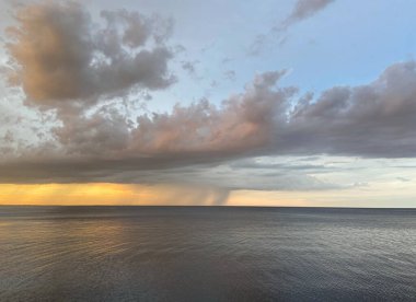 Ufuktaki yağmur duvarının kıyılarından bir görüntü batan güneşin ışınlarıyla ağır bulutları sınırsız deniz yüzeyine bağlıyor..