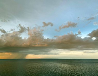 Gök mavisi denizin eşsiz bir görüntüsü. Bulutların altındaki küçük dalgalarla kaplı. Gün batımının renkleriyle aydınlatılmış..