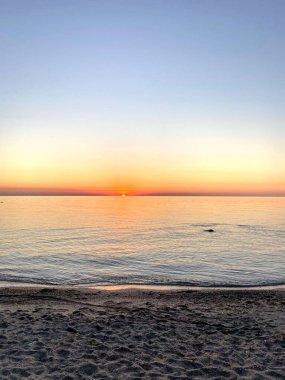 Deniz yüzeyinin kumlu sahilinden inanılmaz bir manzara gökyüzü ufkunda batan güneşin son ışınlarıyla aydınlatılıyor..