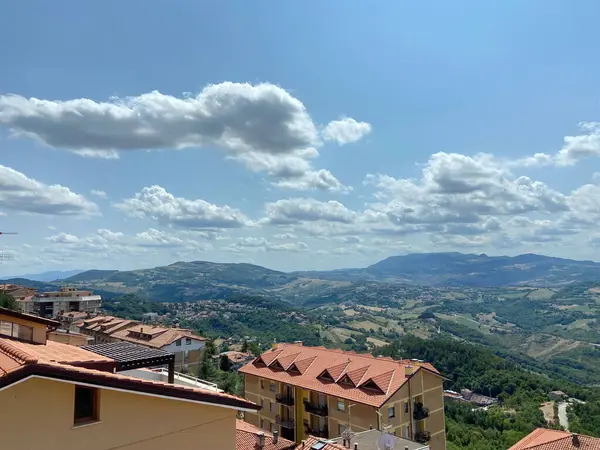Güneşli mavi gökyüzünün manzarası aydınlanmış kar beyazı bulutların desenleriyle süslenmiş San Marino 'nun çatılarından dağ ufkuna doğru süzülüyordu..