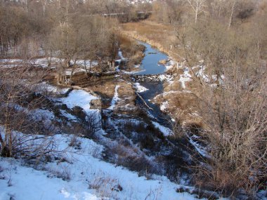Kurumuş sedir ve sazlıklar arasında uzanan ve yapay olarak oluşturulmuş bir barajı geçen bozkır bir nehrin manzarası..