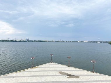 Ufukta bulutlu bir gökyüzünün arka planına karşı şehir binalarıyla kaplı Dnipro setinden karşı kıyıya manzara.