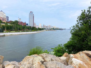 Monastyrsky Adası 'nın kayalık kıyılarından Dinyeper' in diğer kıyısındaki Dnipro gökdelenlerinin bulutlu gri gökyüzünün altında..
