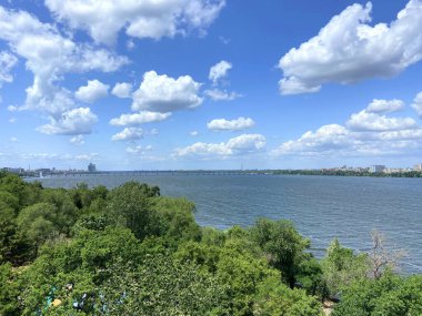 Dnipro boyunca uzanan uzun bir otomobil köprüsünün dönme dolabındaki manzara güneş ışınlarıyla aydınlatılan mavi gökyüzünde bir bulut sürüsüne karşı..