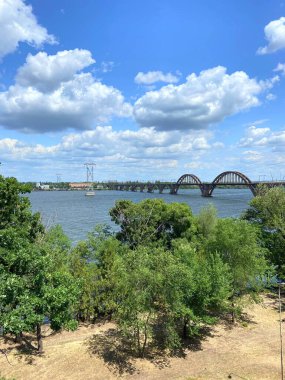 Güneşli bir günde bulutlu mavi gökyüzüne karşı Dnipro boyunca uzanan geniş bir demiryolu köprüsünün dönme dolabından manzara.