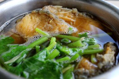 Fried fish(piece) and chinese celery, young ginger slice in broth, Chines style soup in stainless bowl.