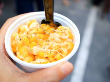 Siyah plastik kaşıkla beyaz bardakta mısır ve peynir..