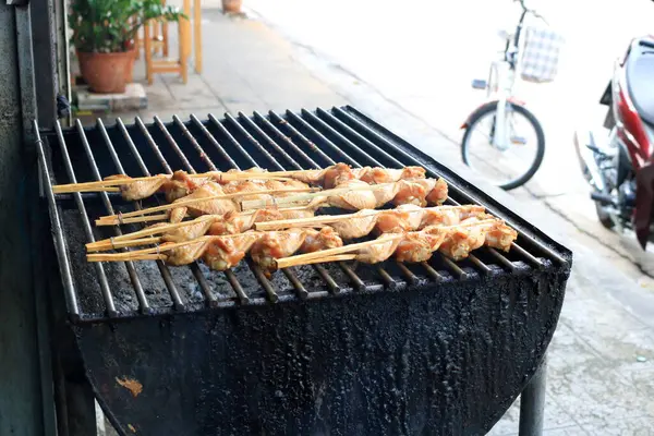 Raw chicken\'s wings marinated sauce clamped bamboo stick on metal retro charcoal stove, Thailand.