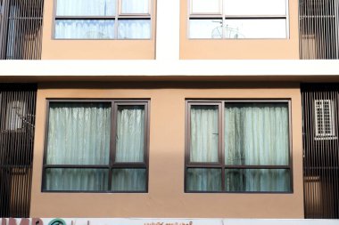 Pencere boyalı cam pencere ve binanın aydınlık duvarında siyah boyalı alüminyum çerçeve, duvarda güneş ışığı ve pencerenin arkasında perde..