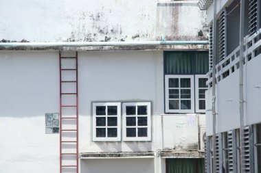 Beyaz pencere, eski ve kirli, tırmalanmış binaların beyaz boyalı duvarlarıyla kaplıydı. Duvarında cam blok olan kırmızı çelik merdiven, Tayland 'da Bankok..