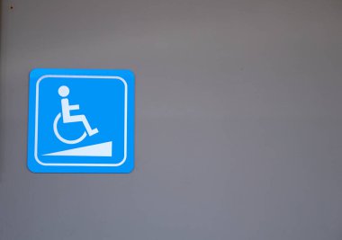 Tekerlekli sandalye için engelli rampasının beyaz işareti açık mavi kare şekilli gri bina duvarı.