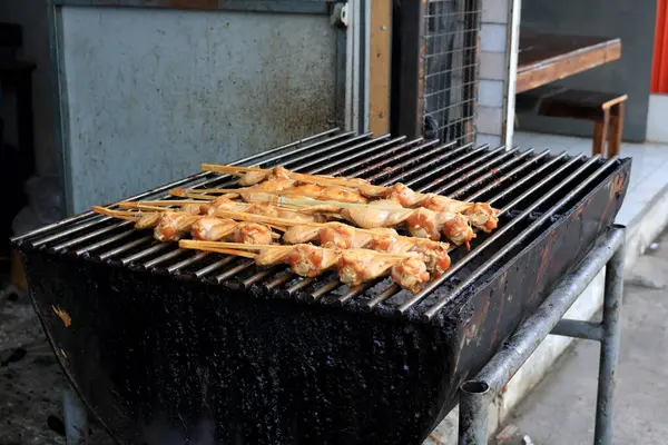 Cooked chicken\'s wings clamped bamboo stick on metal grate of charcoal stove, wings marinate sauce before coolking, Thailand.