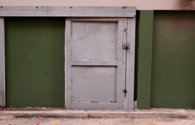 Açık gri boyanmış sadelik ahşap kapı ve beton caddenin yanındaki yeşil bina duvarı..