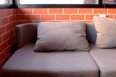 Kahverengi yastık köşedeki kanepede ve turuncu tuğla duvar. Güneş ışığı dışarıdan, cam kanepede..