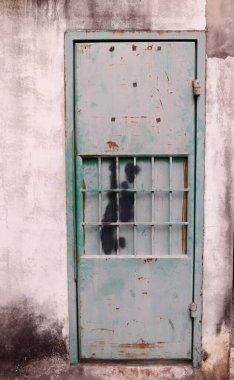 Solgun ve paslı yeşil boyanmış metal kapı ve beton duvar, evin arka kapısı. Tayland 'da kapı ve beton duvarda kirli leke var..