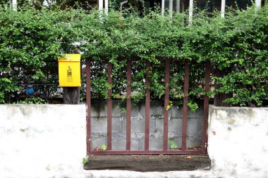 Öndeki binanın yanındaki çitte yeni, parlak, sarı bir posta kutusu..