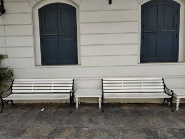 Beton zemin üzerinde beyaz banklar ve Tayland 'da retro tarzı kapalı bina pencereleri olan beyaz duvarlar..