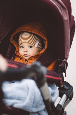 Bebek arabasındaki bebek soğuk bir günde çizgili şapka ve turuncu ceket giyiyor.