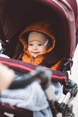Bebek arabasındaki bebek soğuk bir günde çizgili şapka ve turuncu ceket giyiyor.