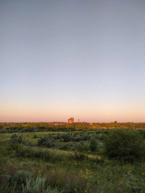 Gün batımında çayırlarda ve ormanlarda sanayi binaları uzakta.