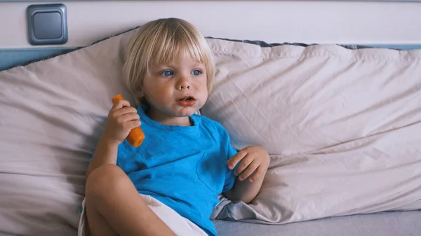 a small child sits on the bed and eats a carrot. High quality 4k footage