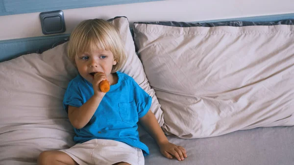 a small child sits on the bed and eats a carrot. High quality 4k footage