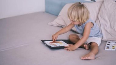 Gri tişörtlü ve şortlu beyaz bir çocuk eskiz defterine renkli kalemler çiziyor. Yüksek kalite 4k görüntü