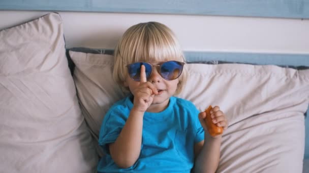 Niño Pequeño Con Gafas Adulto Sienta Cama Come Una Zanahoria — Vídeos de Stock