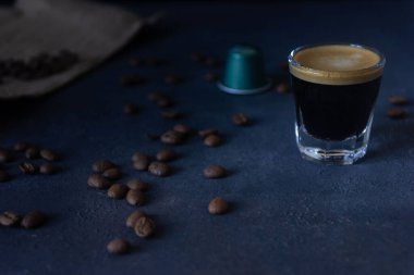 Bir fincan kahve ve bir kapsül, koyu bir zemine dağılmış kahve çekirdekleri, üst görünüm, seçici odak, kopyalama alanı