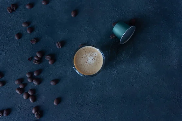 a cup of coffee and a capsule, coffee beans scattered on the dark ground, top view, selective focus, copy space