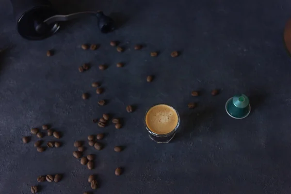 a cup of coffee and a capsule, coffee beans scattered on a dark ground, top view, selective focus, copy space