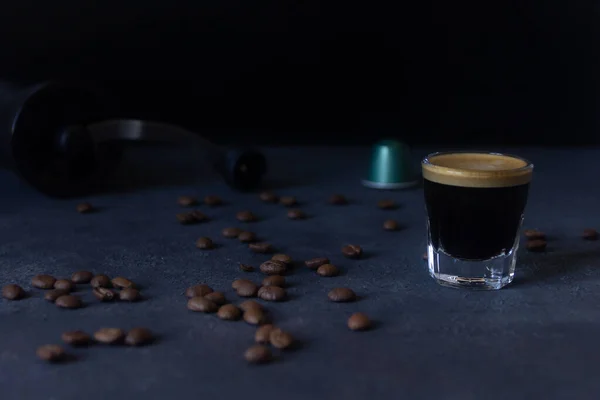 a cup of coffee and a capsule, coffee beans scattered on the dark background, top view, selective focus, copy space