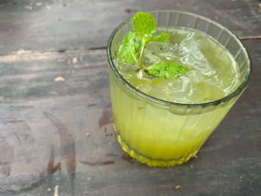 Bir bardak taze yeşil renkli kivi naneli çay ahşap bir masada servis edilir.