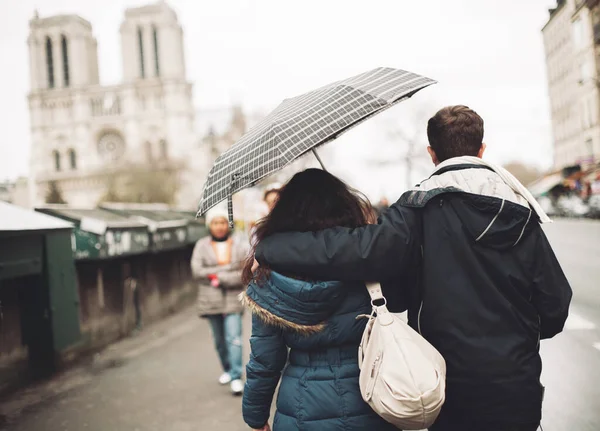 stock image a couple in love walking together under an umbrella in Paris against the backdrop of Notre Dame Cathedral