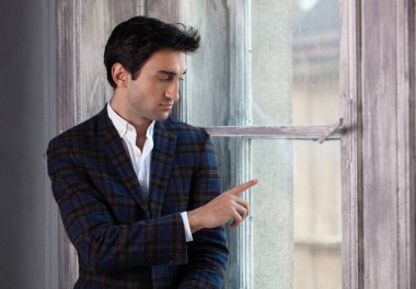 Yakışıklı bir adam pencerenin yanında üzgün elleriyle dokunuyor.