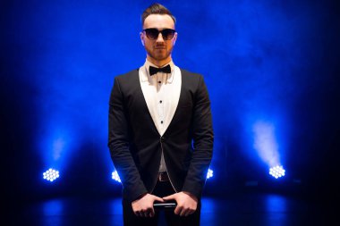 Sahnede mikrofonlu şık bir takım elbise giymiş yakışıklı sunucu ve şovmen