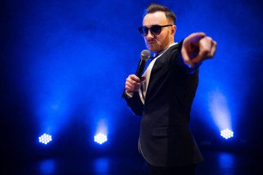 Sahnede mikrofonlu şık bir takım elbise giymiş yakışıklı sunucu ve şovmen