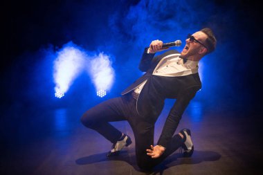 Sahnede mikrofonlu şık bir takım elbise giymiş yakışıklı sunucu ve şovmen