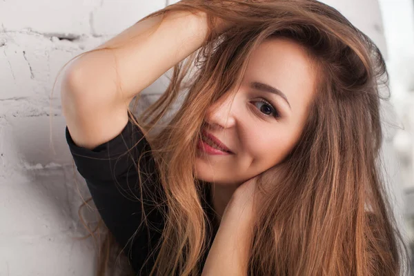 Güzel kız beyaz bir duvarın arkasında gülümsüyor.