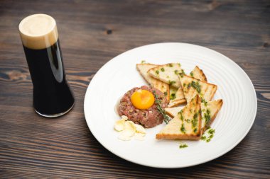 tasty dish of meat and egg yolk with croutons on a plate and a glass of beer, kvass