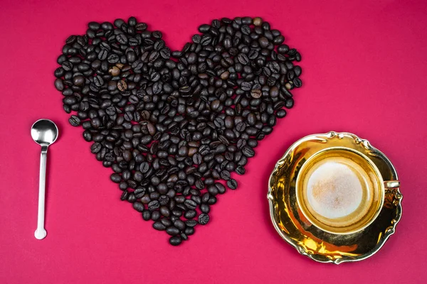 heart  of coffee beans on a pink background with spoon and mug